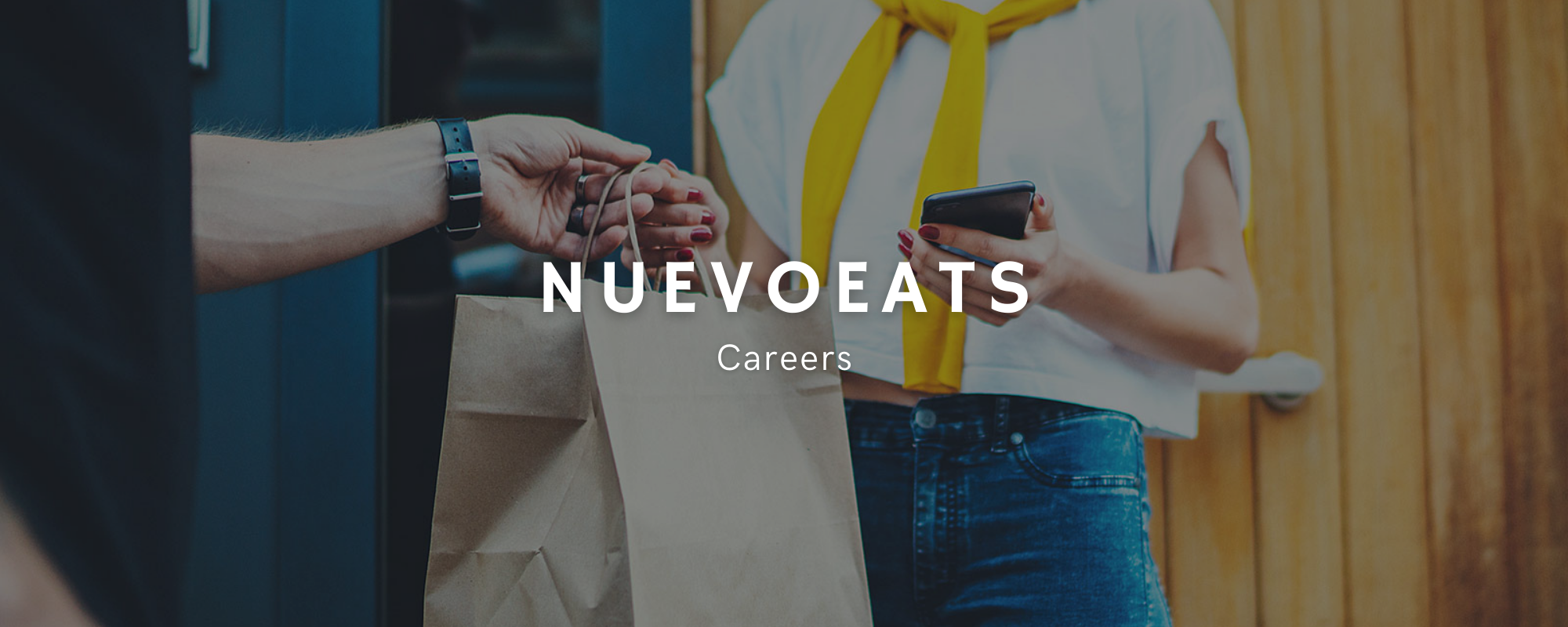 Uma mulher com um celular em uma mão entregando uma sacola de papel a um homem com a outra mão.